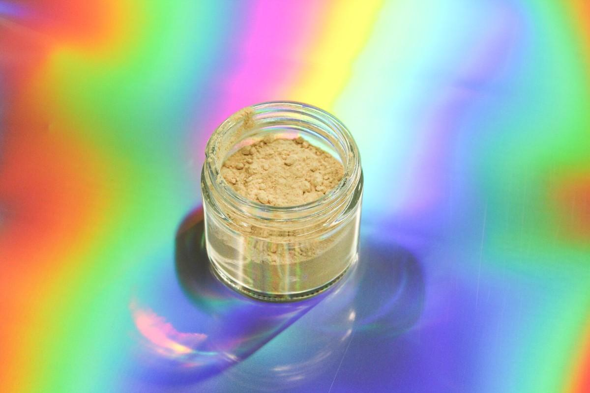 An open glass jar of kanna extract powder on an iridescent surface