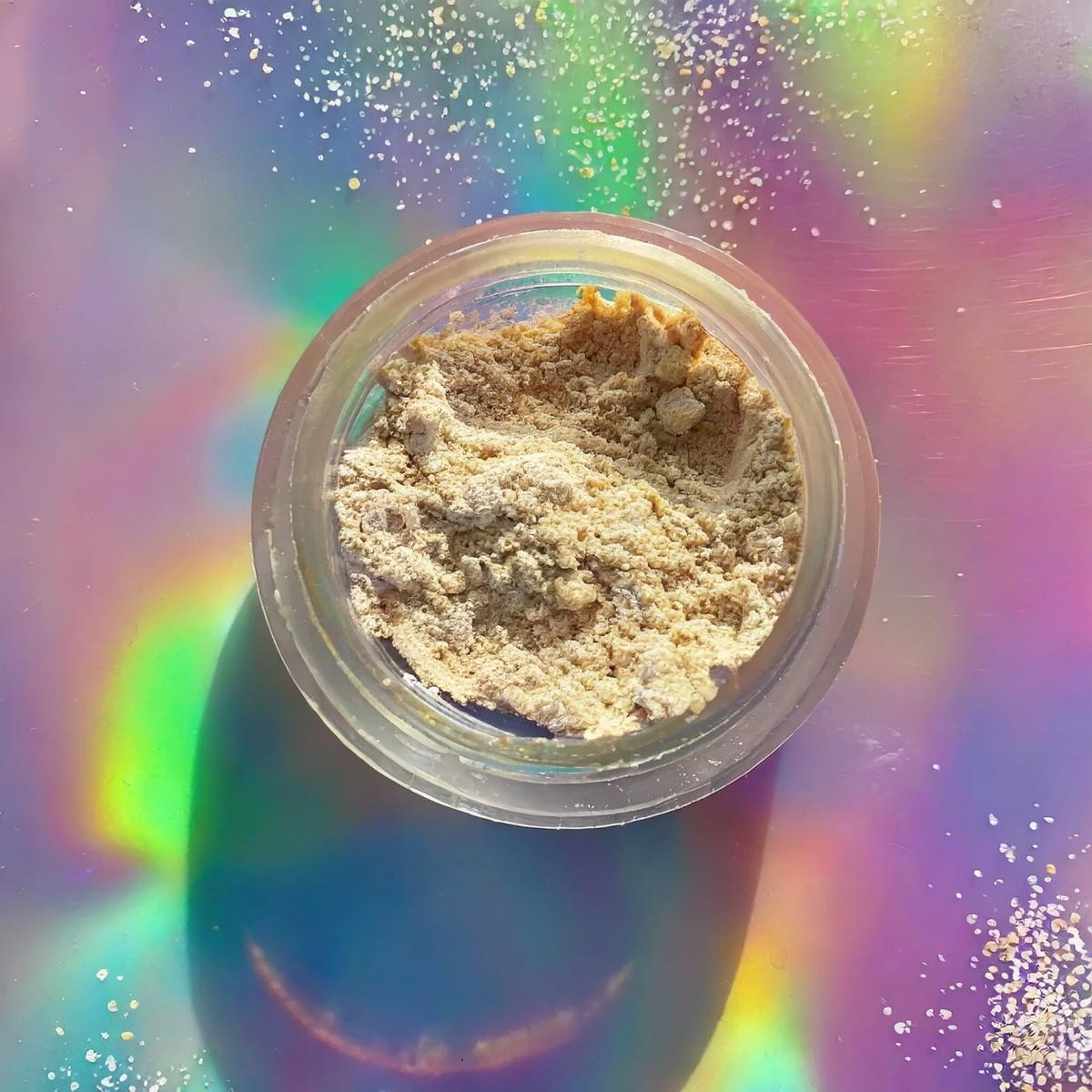 An open glass jar of kanna extract powder photographed from above on an iridescent surface